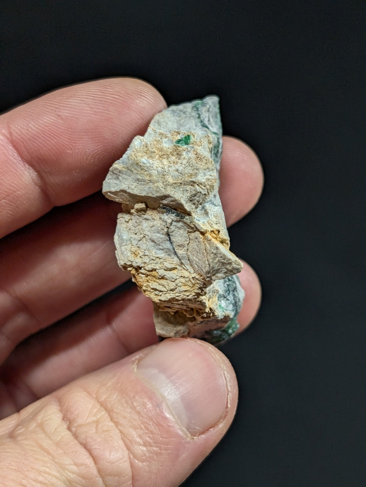 A rough, irregularly shaped mineral specimen with a mottled surface of grayish-white and patches of green and yellow.