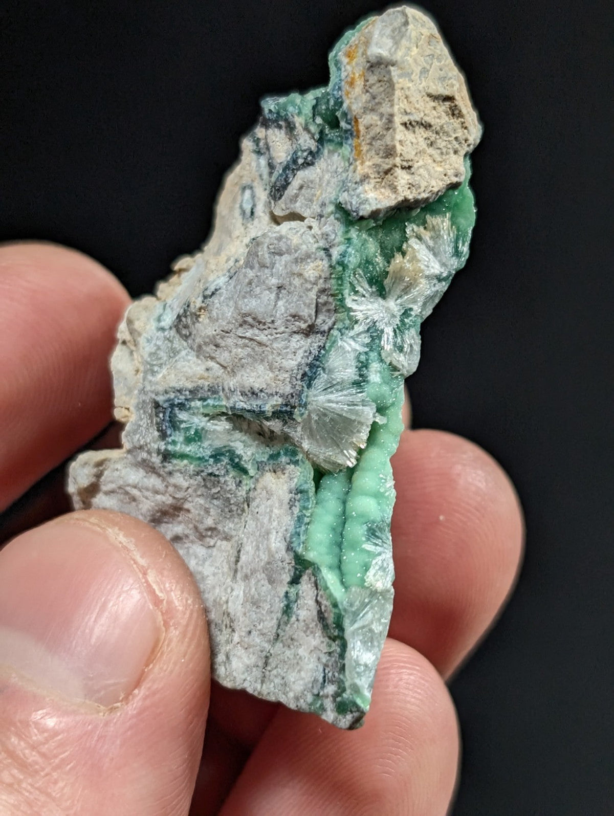 A rough, irregularly shaped mineral specimen featuring vibrant green crystalline formations embedded in a lighter grayish matrix.
