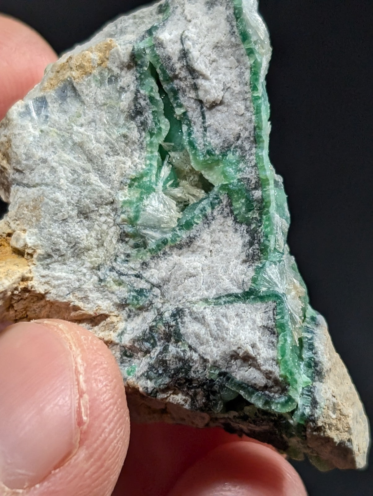 A rough, irregularly shaped piece of green emerald mineral embedded in a grayish matrix.