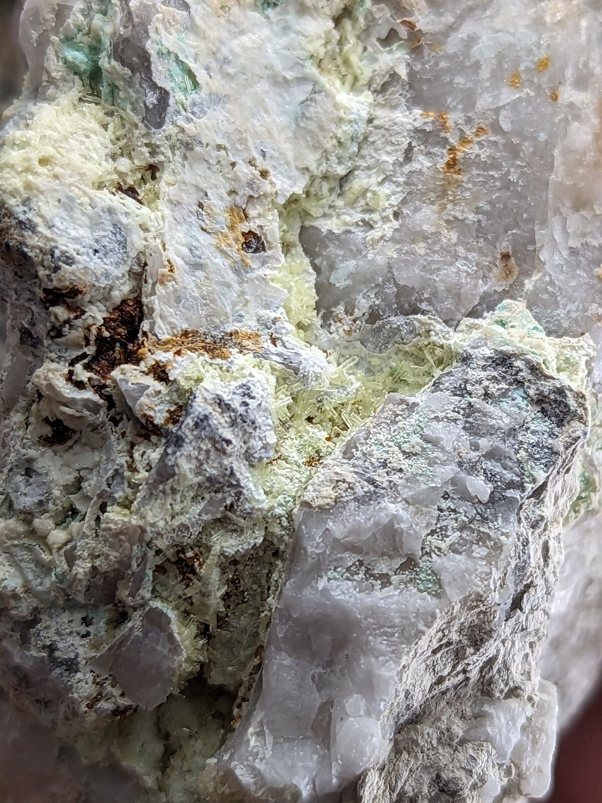 A rugged mineral specimen featuring translucent white and gray crystals interwoven with patches of pale green and earthy brown.