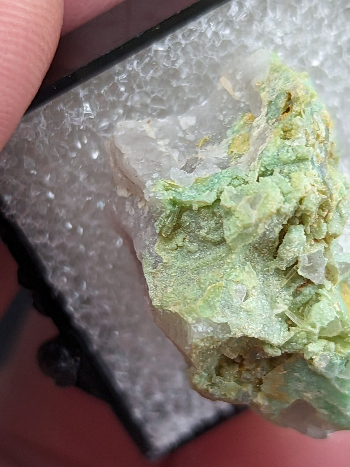 A translucent green mineral specimen with crystalline formations and subtle yellowish patches, displayed in a clear protective case.