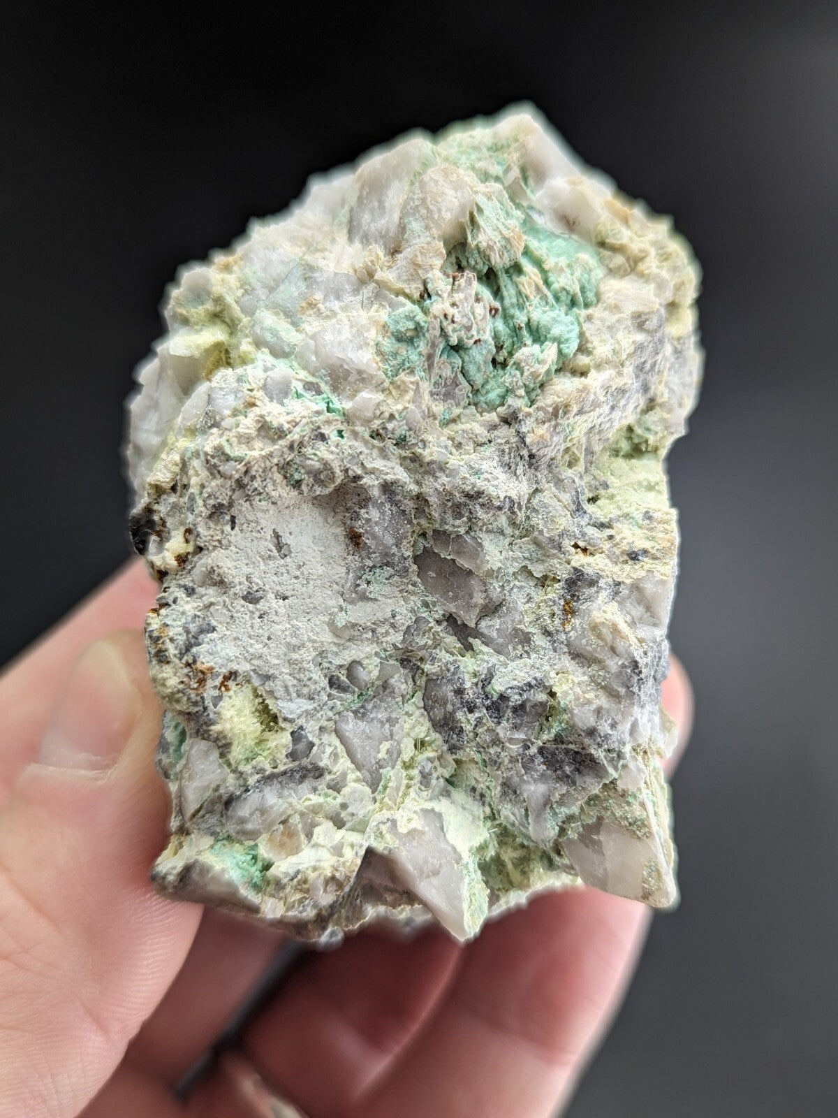A rough, irregularly shaped mineral specimen with a mottled surface of white, gray, and patches of vibrant green.