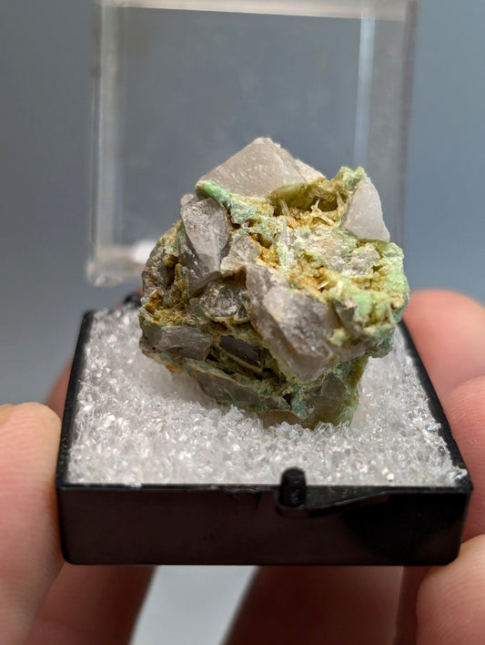 Translucent gray quartz crystal cluster with green and yellow wavellite on variscite in black display case from arkansas