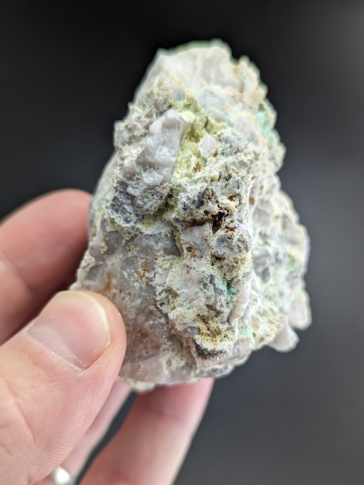 A rough, irregularly shaped mineral specimen with a mix of white and pale green crystalline formations interspersed with darker gray and brown patches.