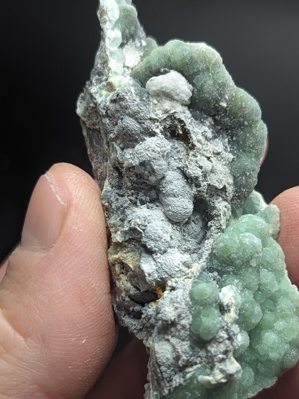 A textured, greenish mineral specimen with a rough, crystalline surface and patches of white material.