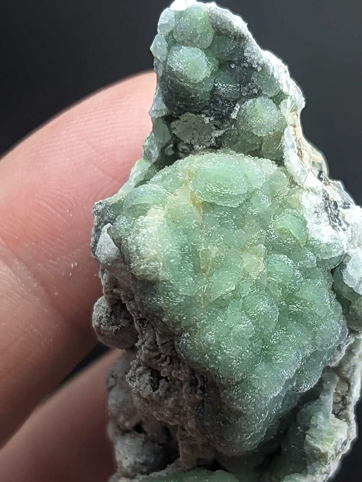 A translucent green mineral specimen with a bumpy, clustered texture and grayish matrix.