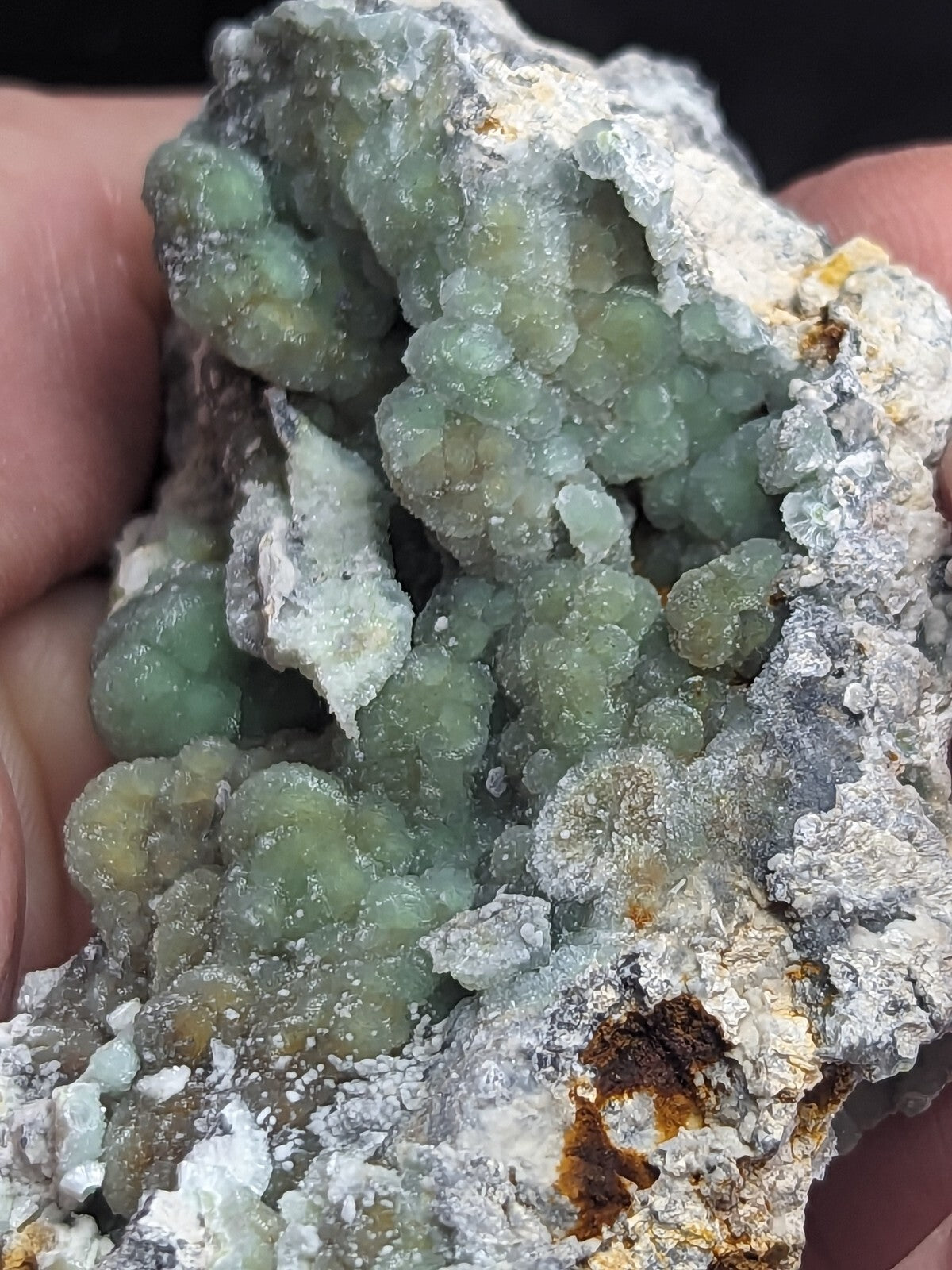 A cluster of translucent green crystals growing on a rough, grayish-white rock matrix.