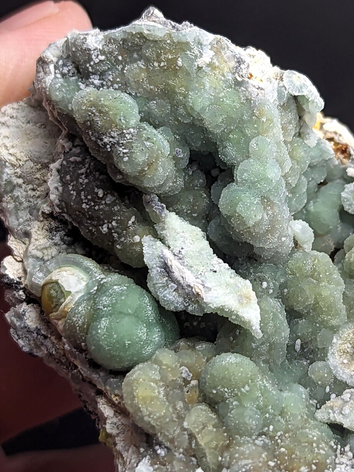A cluster of translucent green crystals with a bumpy, clustered growth pattern and white mineral matrix.