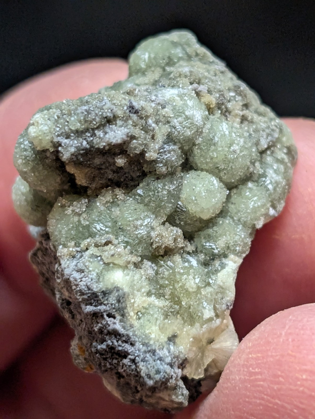 A rough, irregularly shaped mineral specimen with a mix of pale green and grayish hues, featuring clustered crystalline formations.