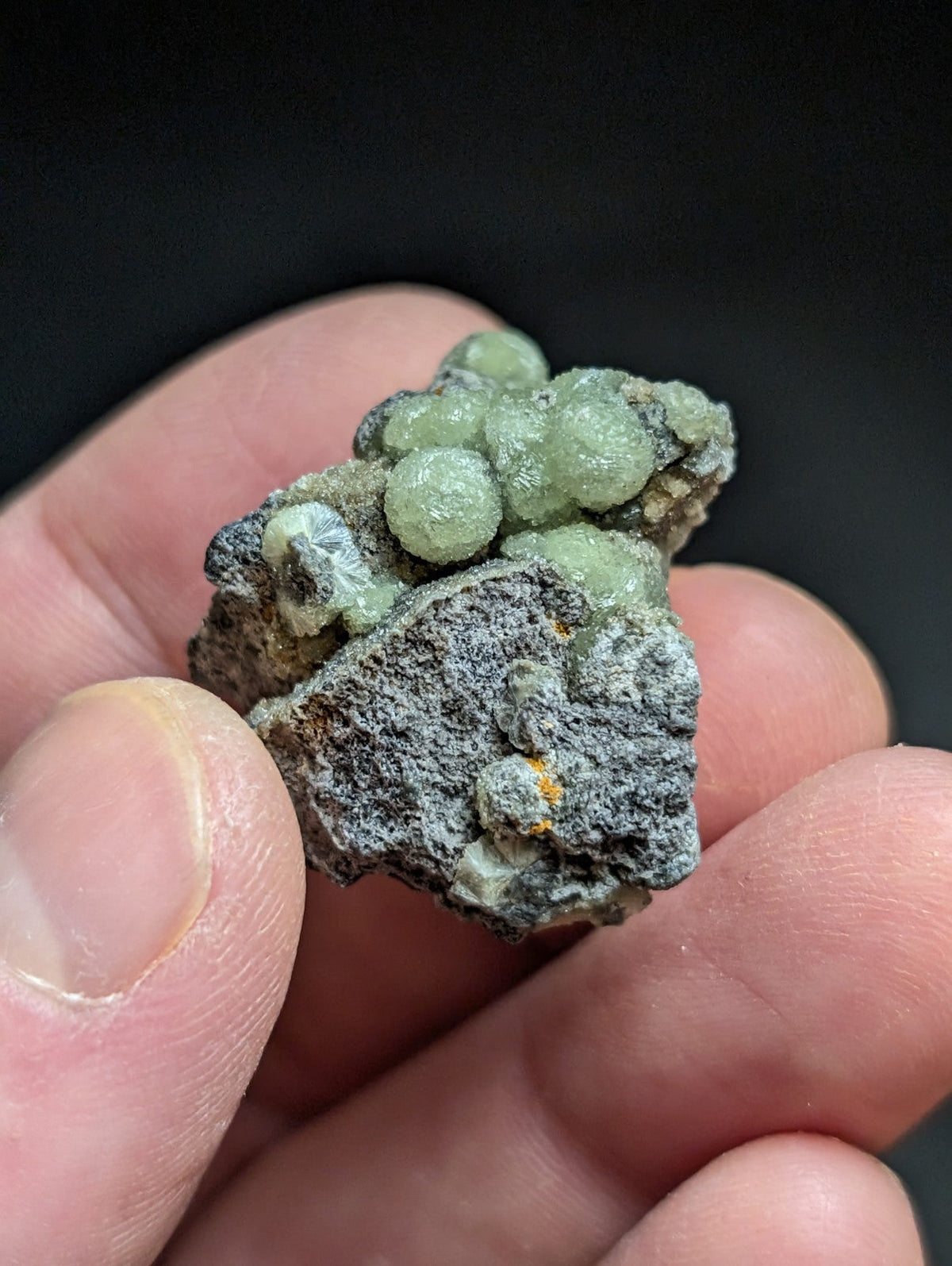 A cluster of translucent green spherical crystals nestled within a rough, grayish rock matrix.