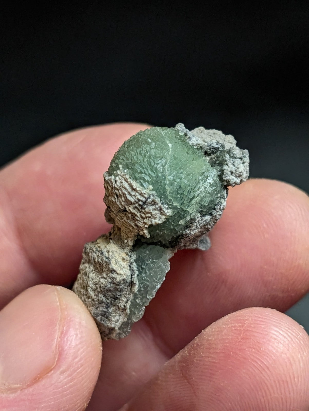 A textured, mossy green mineral specimen with a rough, crystalline surface and grayish patina.