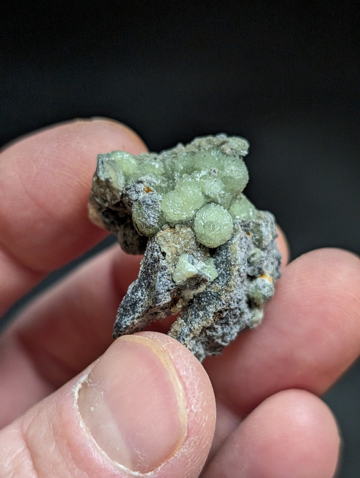 A cluster of translucent green crystals growing from a dark, rough-textured rock matrix.