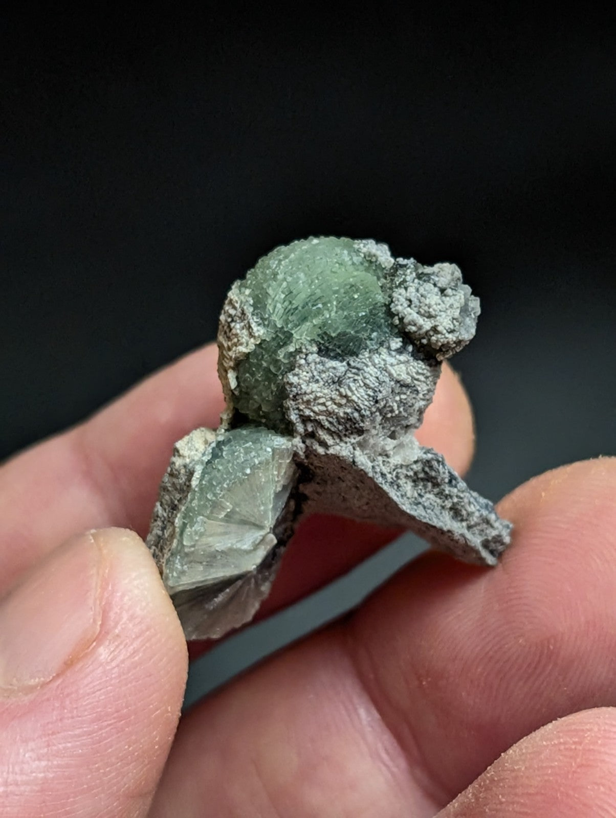 A rough, greenish mineral specimen with a textured surface and visible crystalline formations.