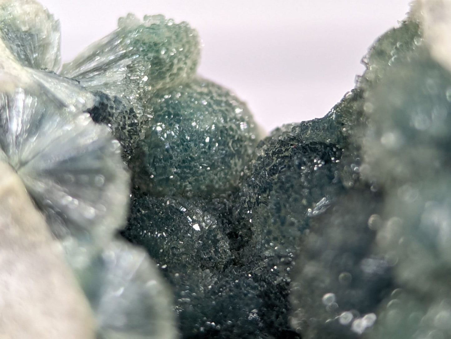 A cluster of translucent green and dark gray mineral crystals with a rough, textured surface.