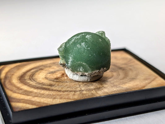 A smooth, deep green jade frog figurine with a slightly weathered texture and natural stone base.