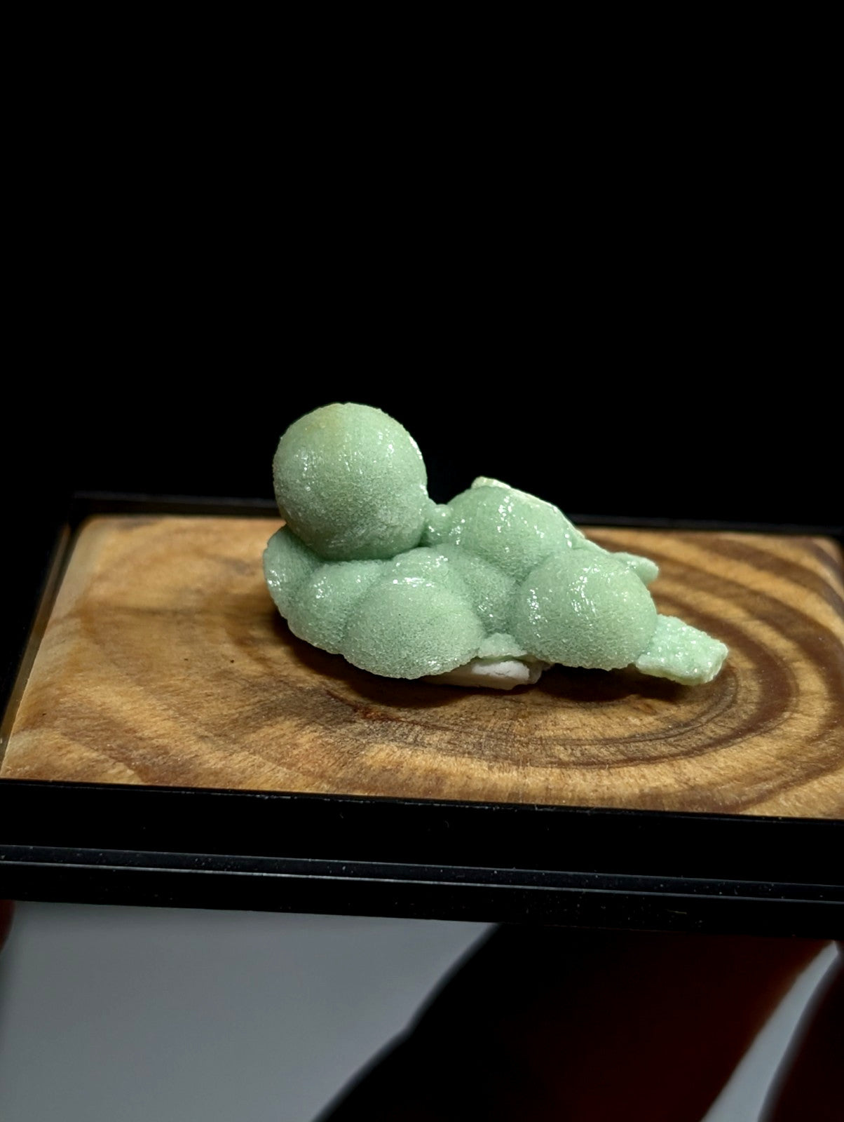 A delicate, light green jade figurine of a reclining figure with rounded, bulbous forms.
