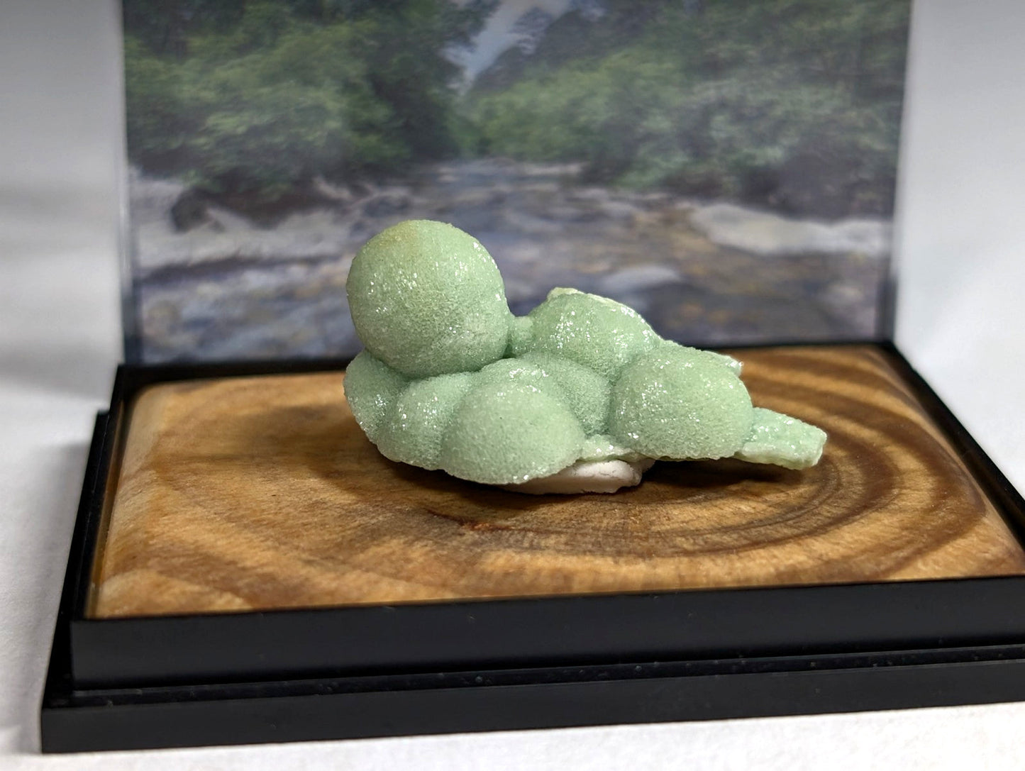 A delicate, pale green crystal formation with a smooth, rounded, and slightly translucent surface rests on a wooden display base.