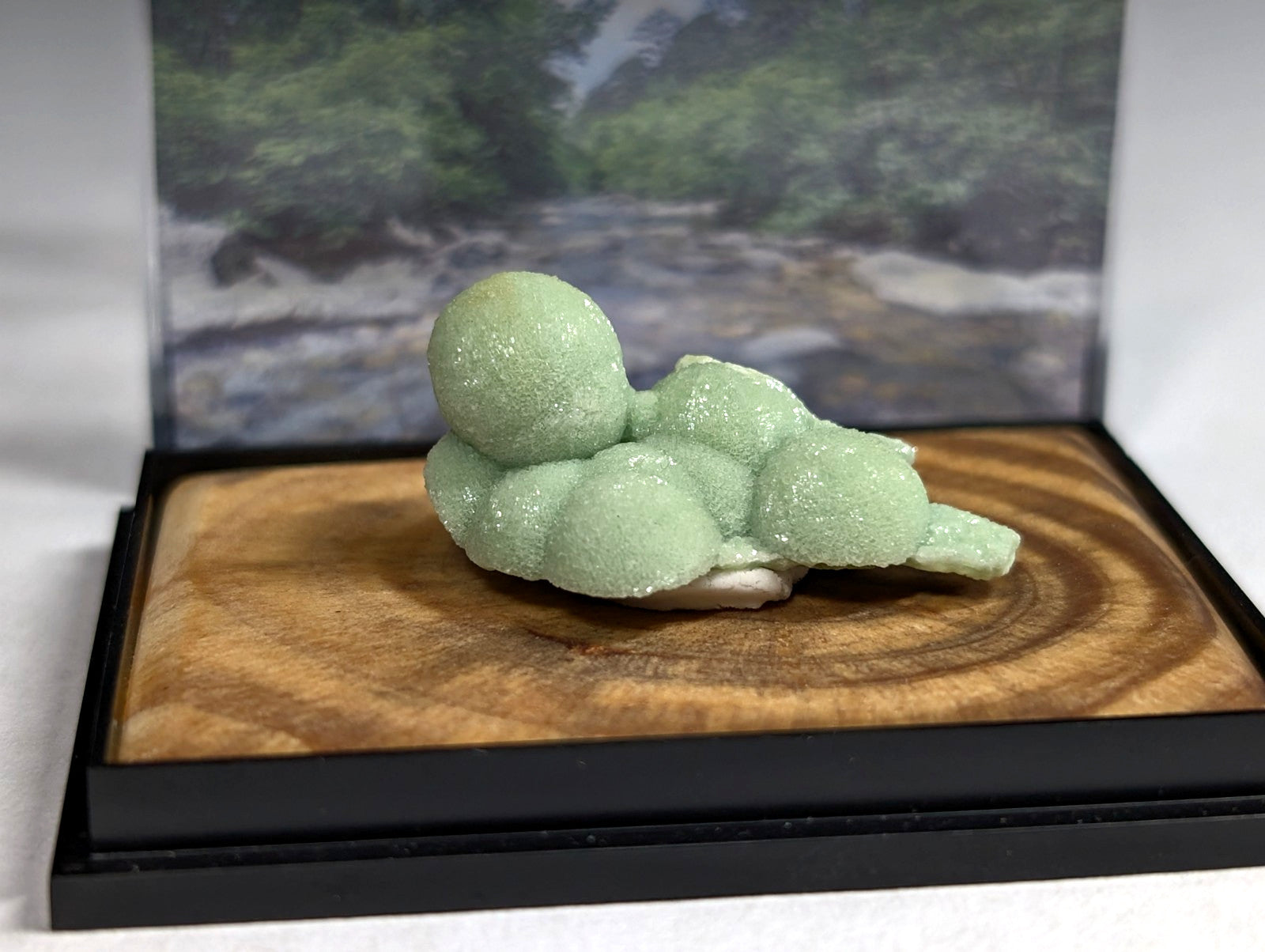 A delicate, pale green crystal formation with a smooth, rounded, and slightly translucent surface rests on a wooden display base.