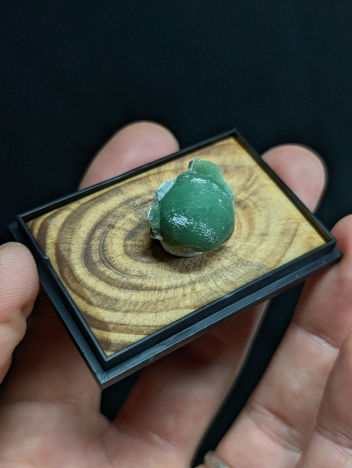 A smooth, translucent green jade stone with a slightly irregular, rounded shape rests on a wooden display tray.