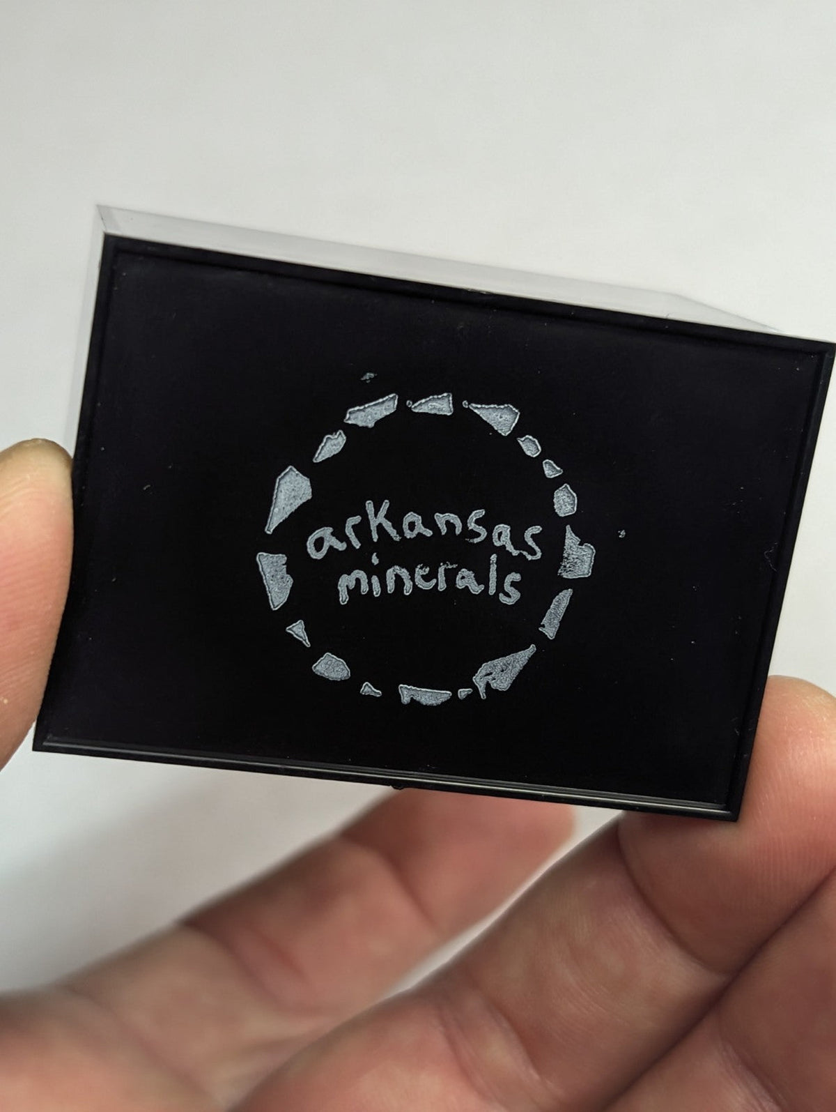 Black rectangular box with silver ’arkansas minerals’ logo and a circular design of stylized mineral fragments.