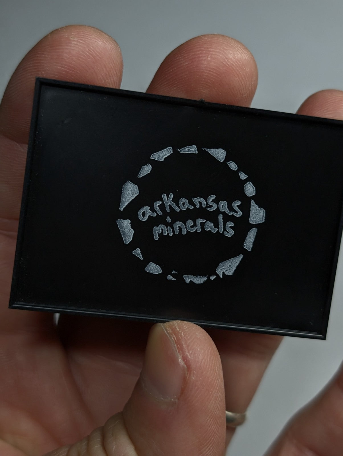 Black rectangular box with silver embossed ’arkansas minerals’ logo encircled by a ring of stylized mineral shapes.