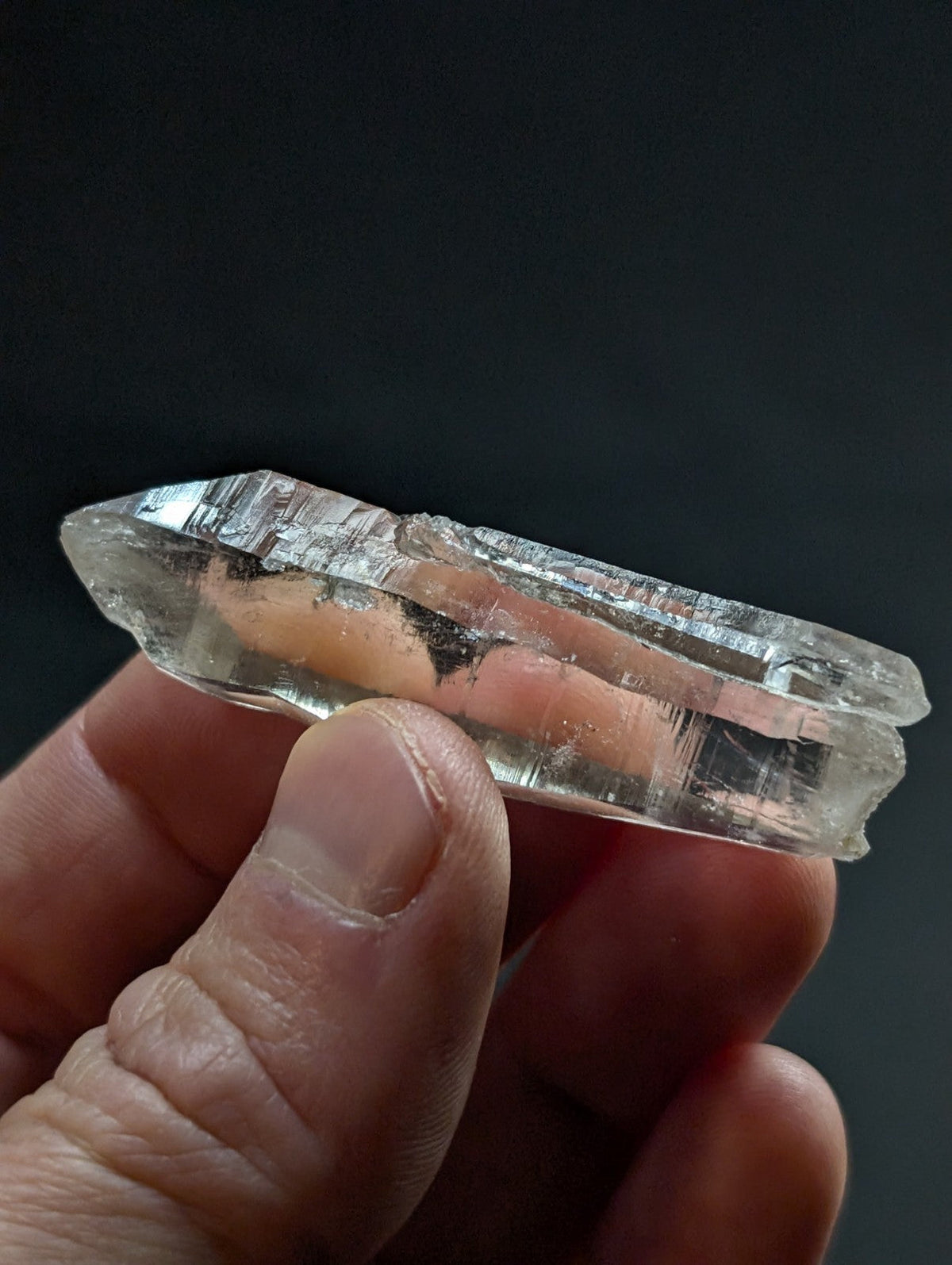 A translucent, clear quartz crystal with natural striations and a pointed tip.