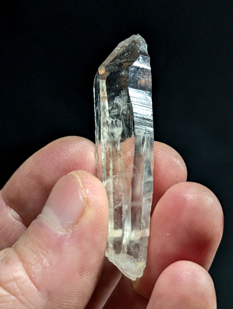 A translucent, clear quartz crystal with a pointed tip and visible internal striations.