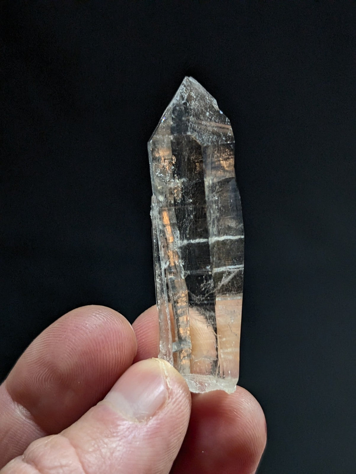A clear, translucent quartz crystal with visible internal striations and a pointed tip.