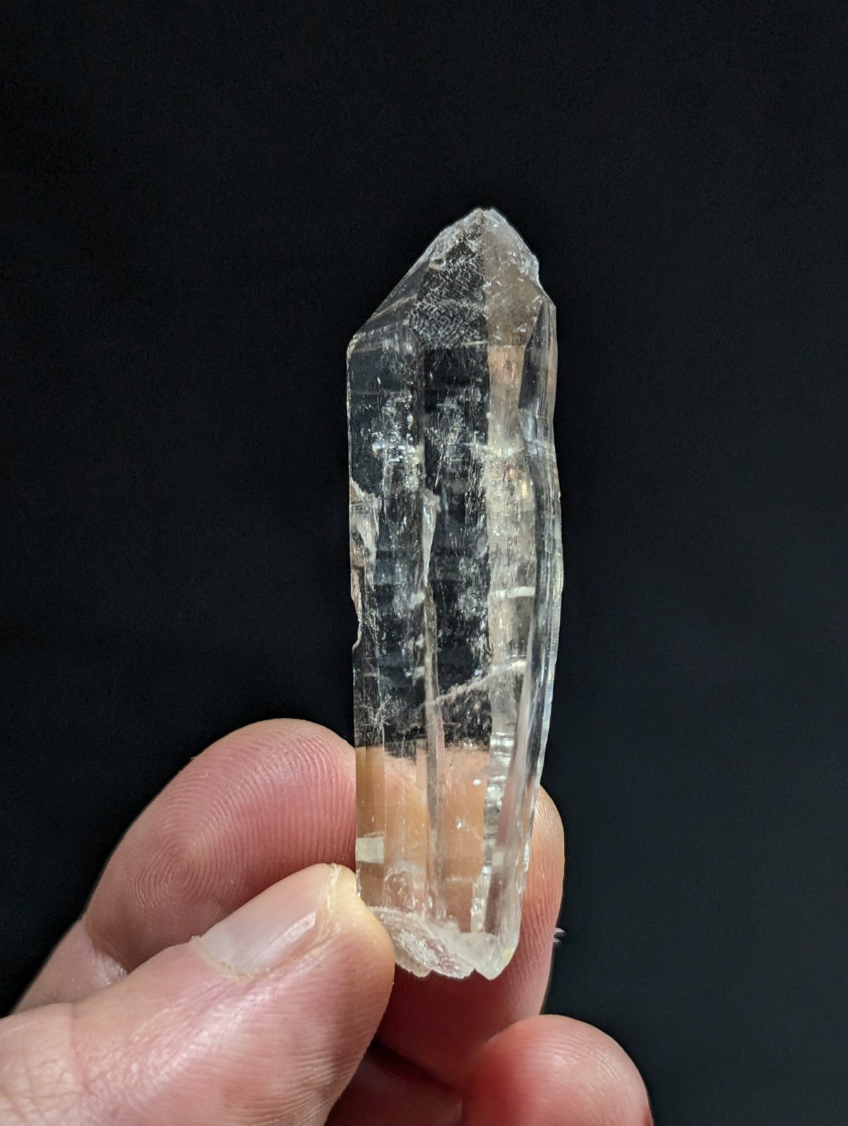 A clear, translucent quartz crystal with visible internal striations and a pointed tip.