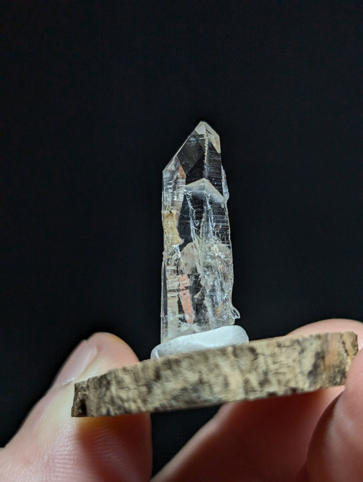 A clear, transparent quartz crystal with a pointed tip and visible internal inclusions, mounted on a rustic wooden base.