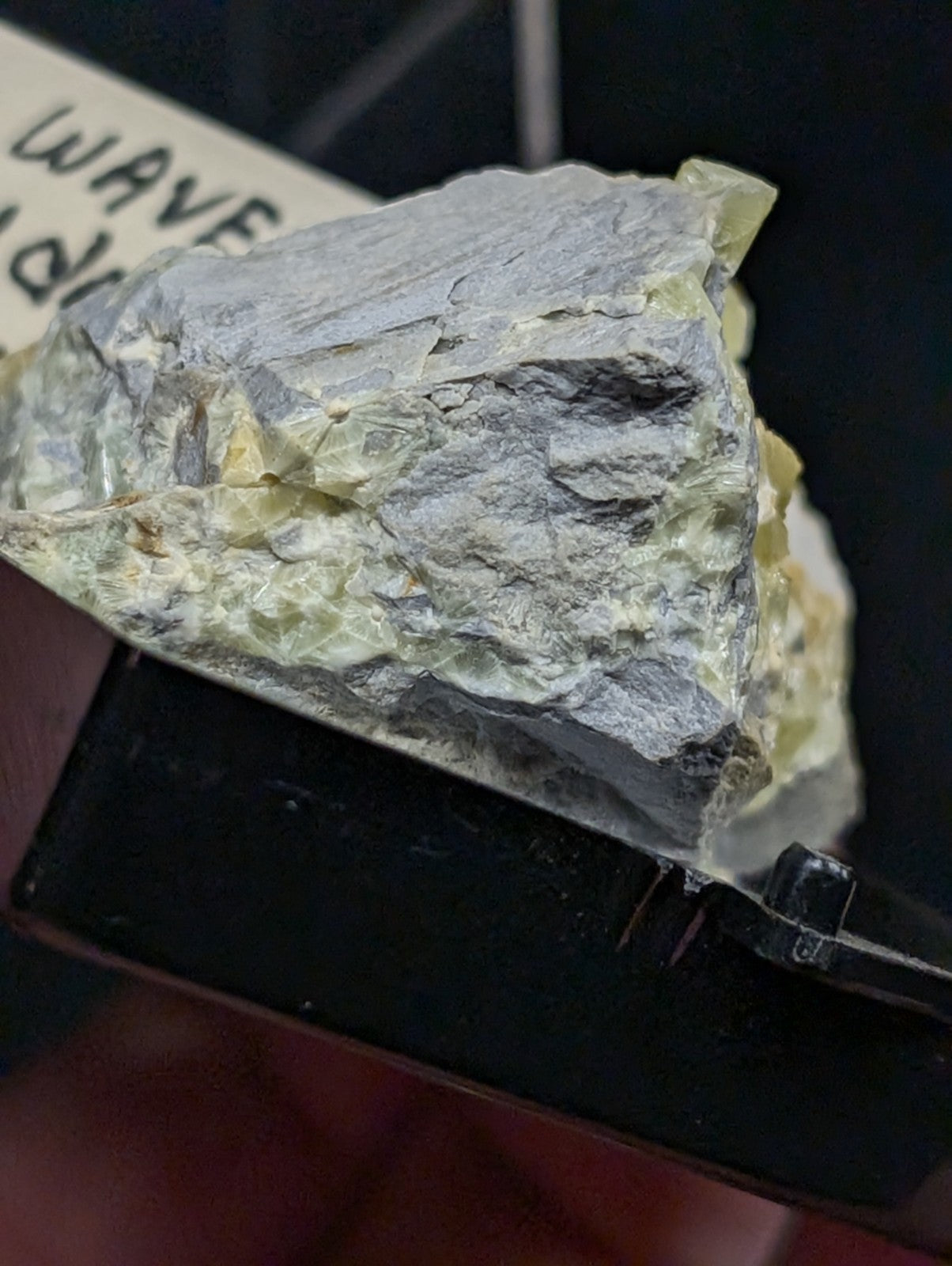 A rough, irregularly shaped mineral specimen with a grayish matrix and patches of translucent yellow-green crystals.